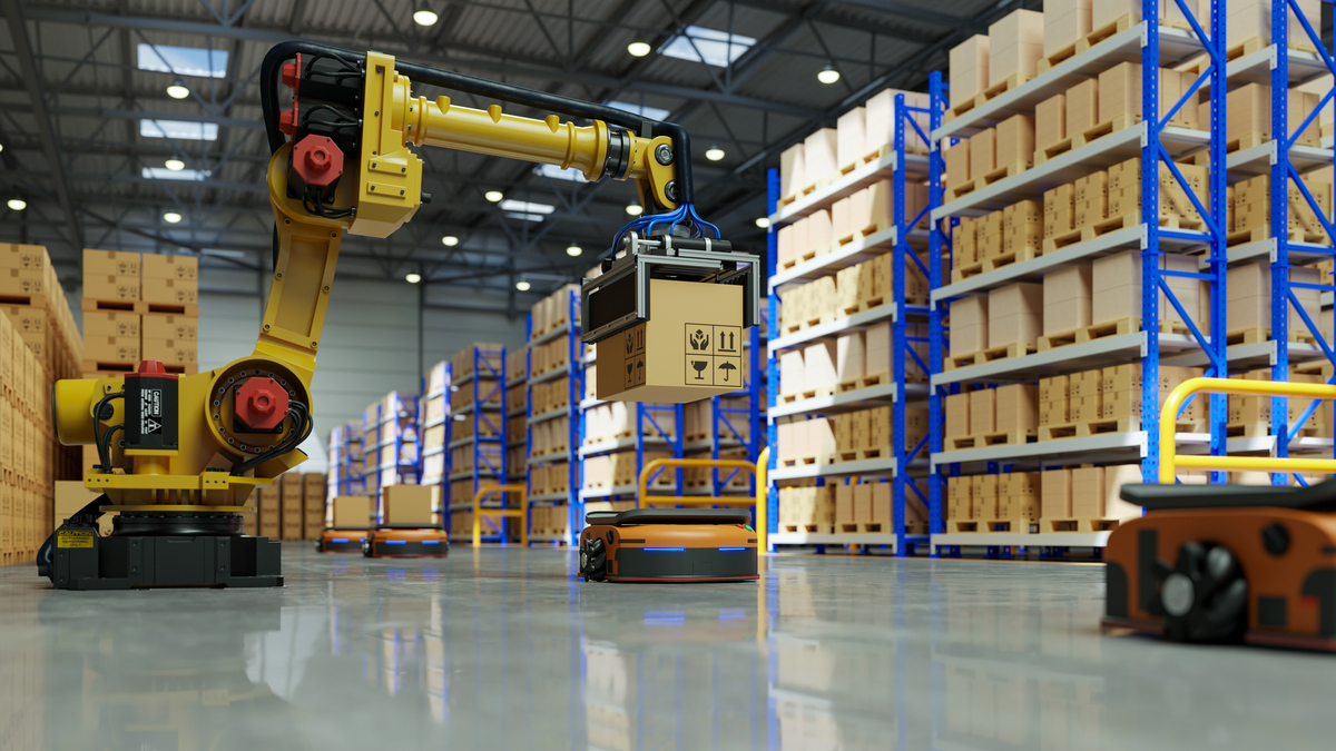 Amazon automated warehouse interior: yellow robotic arm, blue shelving stacked with boxes, robots on shiny floor